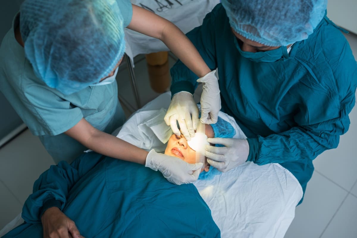 Asistenta plansand un pansament pe ochiul unei paciente dupa operatia de cataracta.